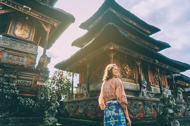 Eine Frau lächelt, während sie zwischen asiatischer, traditioneller Architektur läuft 